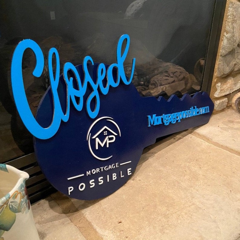 May include: A large, dark blue, key-shaped sign featuring the word "Closed" in bright blue script lettering. The sign displays the white "MP" logo with a house icon, the text "MORTGAGE POSSIBLE" below it, and "Mortgagepossible.com" in blue.