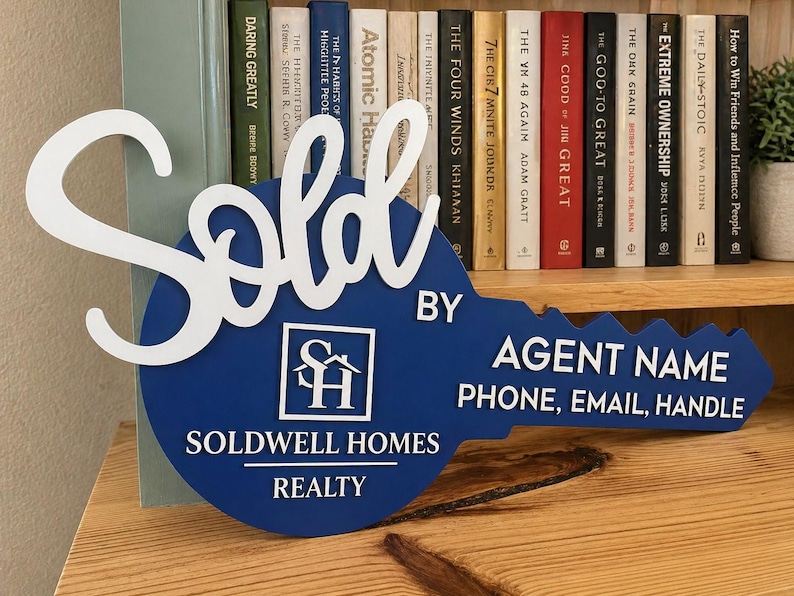 May include: A blue key-shaped sign with white lettering that reads Sold, Soldwell Homes Realty, Agent Name, Phone, Email, Handle, and features a square logo with the letters SH and a house icon in the center of the key head.