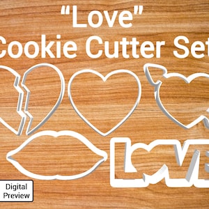 May include: A set of cookie cutters in the shape of hearts, lips, and the word "LOVE". The cutters are white and are shown on a wooden surface. "LOVE" Cookie Cutter Set