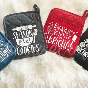 May include: Four Christmas-themed oven mitts with different designs and sayings. The mitts are blue, gray, red, and black. The sayings on the mitts are "Christmas Calories Don't Count", "Tis the Season to Bake Cookies", "Baking Spirits Bright", and "Have a Sweet Christmas".
