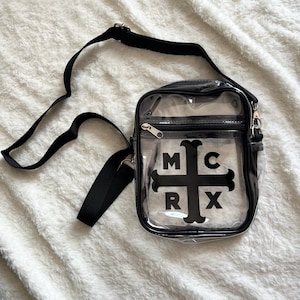 Puede incluir: Un bolso cruzado transparente con una correa y cierre de cremallera negros. El bolso presenta las letras "MCRX" en un dise&ntilde;o de cruz negra en la parte delantera. El bolso est&aacute; hecho de un material transparente.