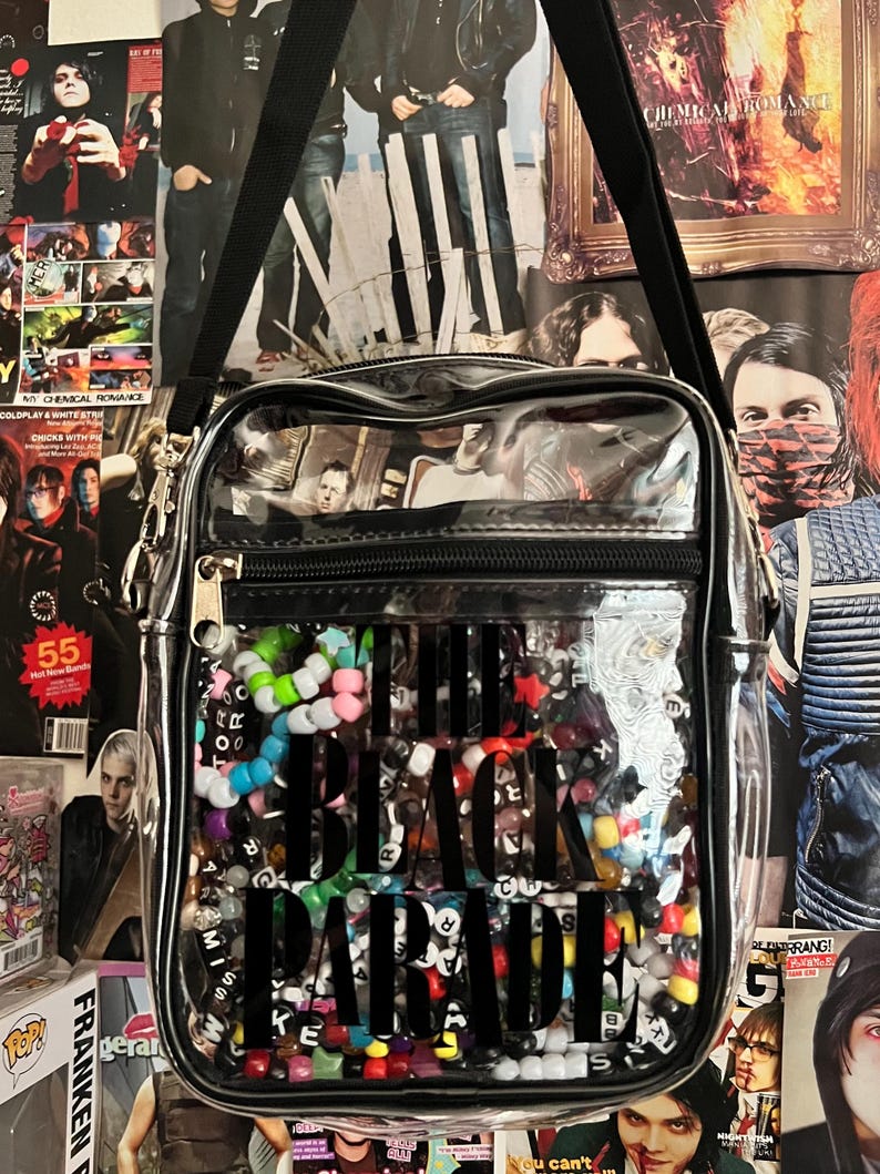 Puede incluir: Bolso bandolera transparente con correa y cremallera negras. La bolsa est&aacute; llena de cuentas de colores y las palabras "THE BLACK PARADE" en letras negras grandes. Carteles en el fondo.