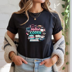 May include: Black t-shirt with a colorful graphic that reads "Medical Coder." The design includes a stethoscope, computer, pills, coffee cup, and binary code. The shirt is made of a soft material.