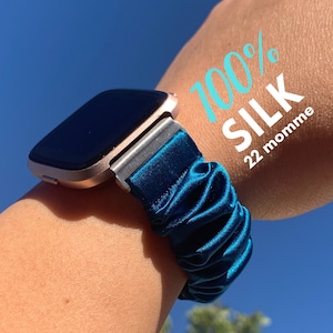 May include: A teal blue 100% silk watch band with a rose gold watch face. The band is made of 22 momme silk.