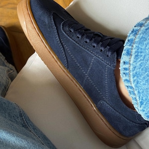 Puede incluir: Zapatillas de ante azul marino con suela de goma marr&oacute;n. Las zapatillas tienen un dise&ntilde;o de perfil bajo con un patr&oacute;n de diamantes cosido en el lateral. Los cordones y la leng&uuml;eta son azul marino.