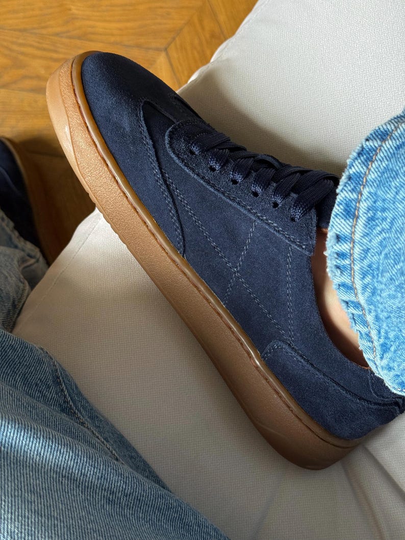 Puede incluir: Zapatillas de ante azul marino con suela de goma marr&oacute;n. Las zapatillas tienen un dise&ntilde;o de perfil bajo con un patr&oacute;n de diamantes cosido en el lateral. Los cordones y la leng&uuml;eta son azul marino.