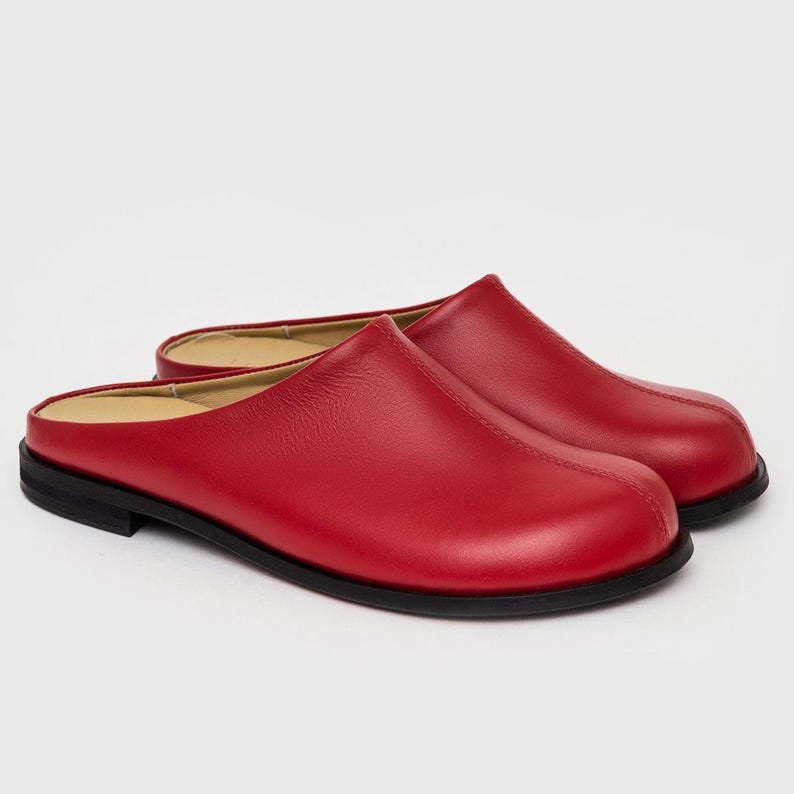 May include: A pair of red leather clogs with a rounded toe and a black sole. The shoes have a slip-on design and are made of smooth, shiny leather. The clogs are a vibrant shade of red.