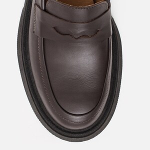 K&ouml;nnte beinhalten: Nahaufnahme eines braunen Lederloafers mit dicker schwarzer Sohle. Der Schuh hat ein klassisches Penny-Loafer-Design mit einem dekorativen Riemen. Die Sohle ist etwa 2,5 cm dick.