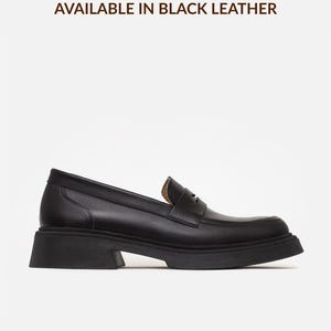 Może przedstawiać: Czarny sk&oacute;rzany mokasyn z grubą, teksturowaną gumową podeszwą i klasycznym paskiem z wycięciem na podbiciu. Tekst "AVAILABLE IN BLACK LEATHER" znajduje się nad butem, a "*also available in other colors" znajduje się poniżej.