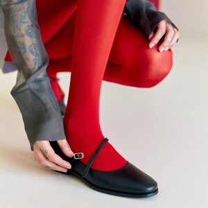 Puede incluir: Una persona con medias rojas y zapatos de cuero negro con una correa de hebilla. Los zapatos tienen una punta puntiaguda y un tac&oacute;n bajo.