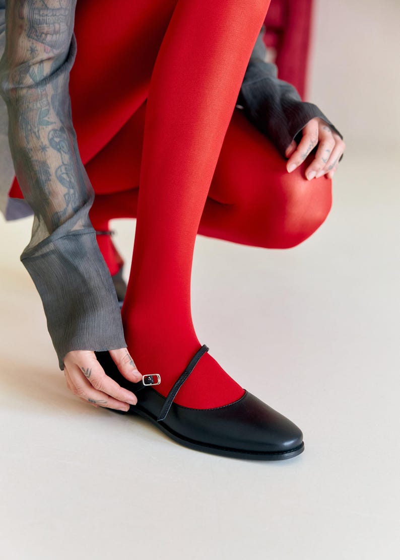 Puede incluir: Una persona con medias rojas y zapatos de cuero negro con una correa de hebilla. Los zapatos tienen una punta puntiaguda y un tac&oacute;n bajo.