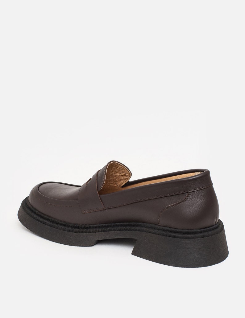 K&ouml;nnte beinhalten: Ein brauner Lederloafer mit dicker schwarzer Sohle. Der Schuh hat eine runde Spitze und ein klassisches Penny-Loafer-Design. Die Sohle ist etwa 5 cm dick.