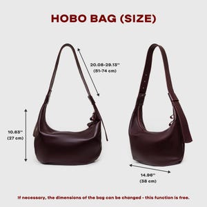 May include: Two burgundy hobo bags are displayed, showcasing their dimensions. The bags have adjustable straps and a curved design. The text "HOBO BAG (SIZE)" is at the top. The dimensions are 10.63" (27 cm), 20.08-29.13" (51-74 cm), and 14.96" (38 cm).