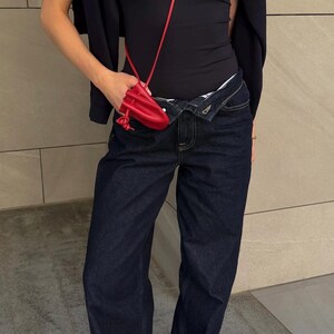 May include: A person wearing a black tank top, dark blue jeans, and red shoes. A red purse hangs from the shoulder. A dark blue jacket is draped over the shoulders.