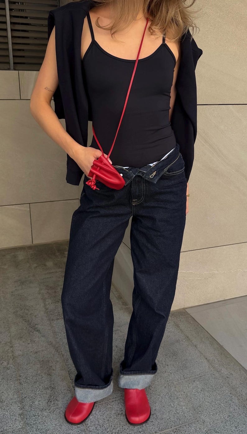 May include: A person wearing a black tank top, dark blue jeans, and red shoes. A red purse hangs from the shoulder. A dark blue jacket is draped over the shoulders.