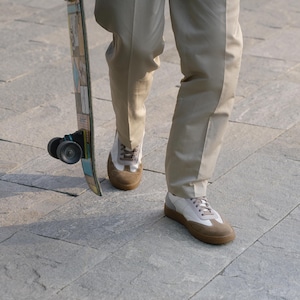 May include: A person holding a skateboard with a colorful design. The person is wearing tan pants and white and brown sneakers. The skateboard has black wheels.