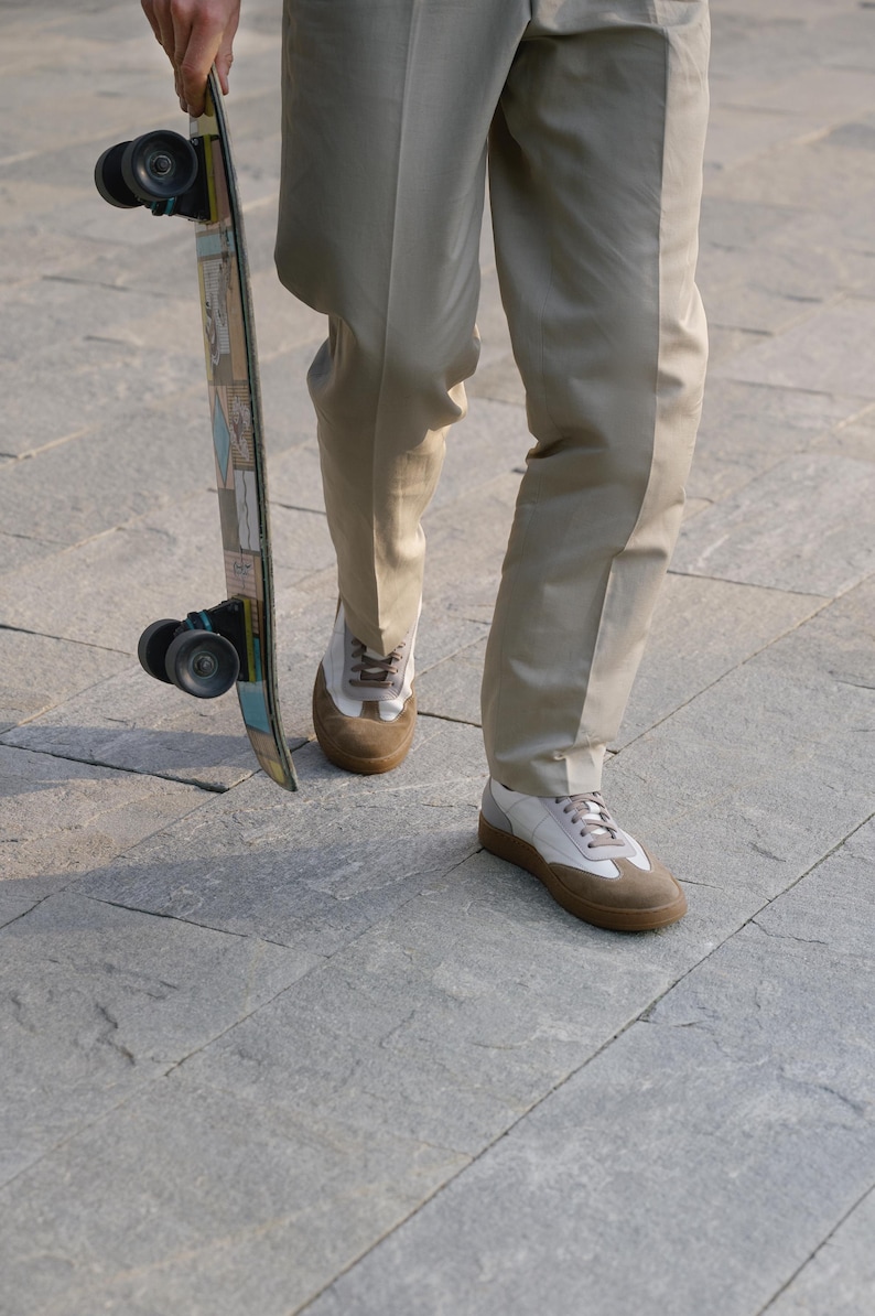 May include: A person holding a skateboard with a colorful design. The person is wearing tan pants and white and brown sneakers. The skateboard has black wheels.