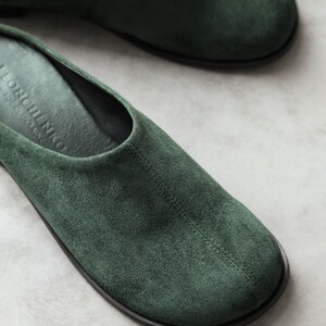 May include: A pair of dark green suede slip-on shoes with a rounded toe and a centre seam. The interior footbed is black and features the embossed text "LEONCHENKO" and "MADE IN UKRAINE" near the heel area, with a thin black outer sole.
