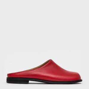 May include: A single red leather mule with a rounded toe and a low, black sole. The shoe has a simple, minimalist design and a smooth texture. The heel is approximately 1 inch high.