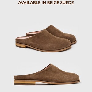 May include: A pair of brown suede mules with a rounded toe, a low heel, and a light-coloured interior lining. The text "AVAILABLE IN BEIGE SUEDE" and "*also available in other colours" is visible above and below the shoes respectively.
