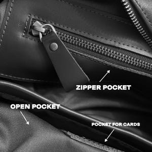May include: Close-up of a black leather bag interior with multiple compartments. Features include a zippered pocket, an open pocket, and a pocket for cards. The bag has a sleek, minimalist design with visible stitching and a leather zipper pull.