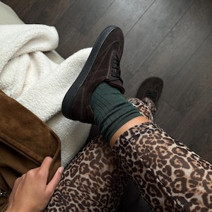 Puede incluir: Primer plano de una zapatilla de ante marr&oacute;n con suelas y cordones negros. El zapato se combina con calcetines verdes de canal&eacute; y leggings con estampado de leopardo. La imagen est&aacute; tomada desde arriba.