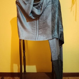 May include: A light blue and black patterned shawl with a fringe on the bottom. The shawl is draped over a wooden stand.