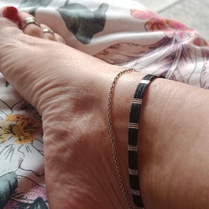 Op de afbeelding: Een close-up van een enkel met twee enkelbandjes. Een enkelbandje is een dunne zilveren ketting en de andere is een zwarte en zilveren kralen enkelband.