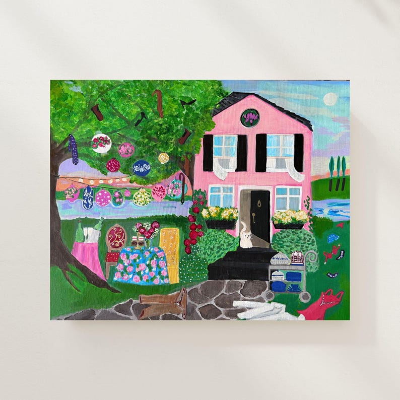 May include: A whimsical painting of a pink house with black shutters and a black door. The yard is decorated with colorful hanging ornaments and a table with a floral tablecloth. A white cat sits on the porch.