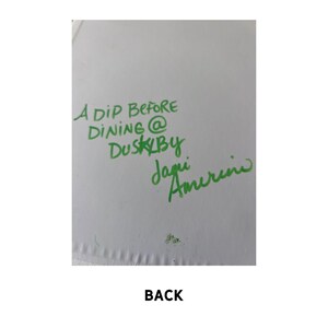 May include: A white card with green handwritten text that reads "A Dip Before Dining @ Dusk By Jagi Amerine". The word "BACK" is printed in black at the bottom of the card.