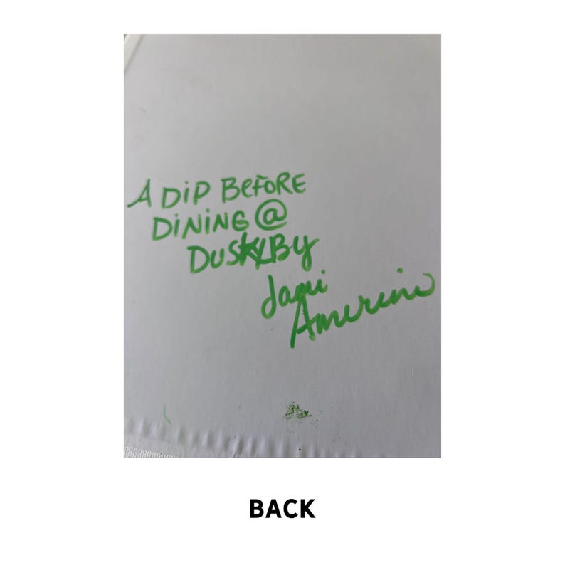 May include: A white card with green handwritten text that reads "A Dip Before Dining @ Dusk By Jagi Amerine". The word "BACK" is printed in black at the bottom of the card.