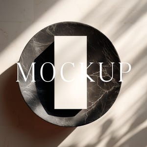 May include: A top-down view of a black and gray marble-patterned round surface with a white rectangular card in the center. The word "MOCKUP" is displayed in white letters across the card. Shadows from foliage are cast on the surface.
