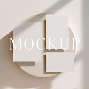 May include: A mockup featuring three blank white cards arranged on a beige, circular plate. The word "MOCKUP" is displayed in a light font across the cards. The scene is lit with soft, natural light, casting shadows.