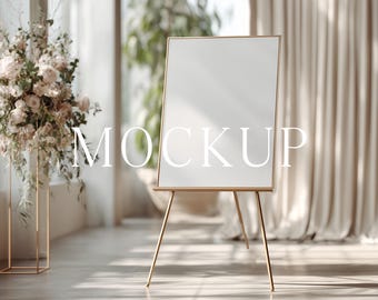 May include: A blank white sign on a gold easel, with the word "MOCKUP" in white text. The sign is in a bright room with a floral arrangement and draped curtains.