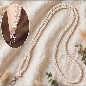 May include: A long lanyard made of white spherical pearls strung together, featuring a silver-toned metal lobster clasp at the end. An inset circular image shows the pearl lanyard attached to a brown garment with the silver clasp.