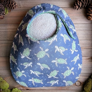 May include: A blue fabric bag with a turtle pattern. The bag has a white interior and a green trim around the opening. The turtles are green and white, and the background is a dark blue color.