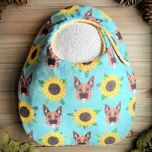May include: A turquoise blue fabric baby bib with a yellow trim and a pattern of German Shepherd dog faces and sunflowers.