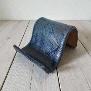 May include: A blue ceramic soap dish with a wave-like design. The dish has a textured surface with a dark blue glaze and a lighter blue pattern. The dish is approximately 6 inches long and 4 inches wide.