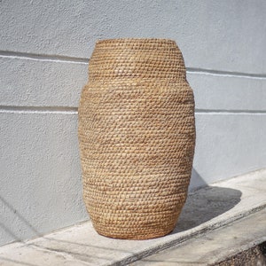 May include: A large, woven, tan-colored basket with a rounded shape. The basket is made of natural materials and has a textured surface.