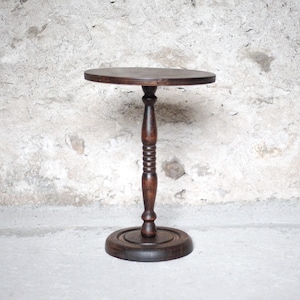 Op de afbeelding: Een donkerbruine houten zuiltafel met een rond blad, een centrale gedraaide kolom met decoratieve ribbels en een stevige ronde voet. De tafel heeft een gladde, gepolijste afwerking die de natuurlijke houtnerf goed laat uitkomen.