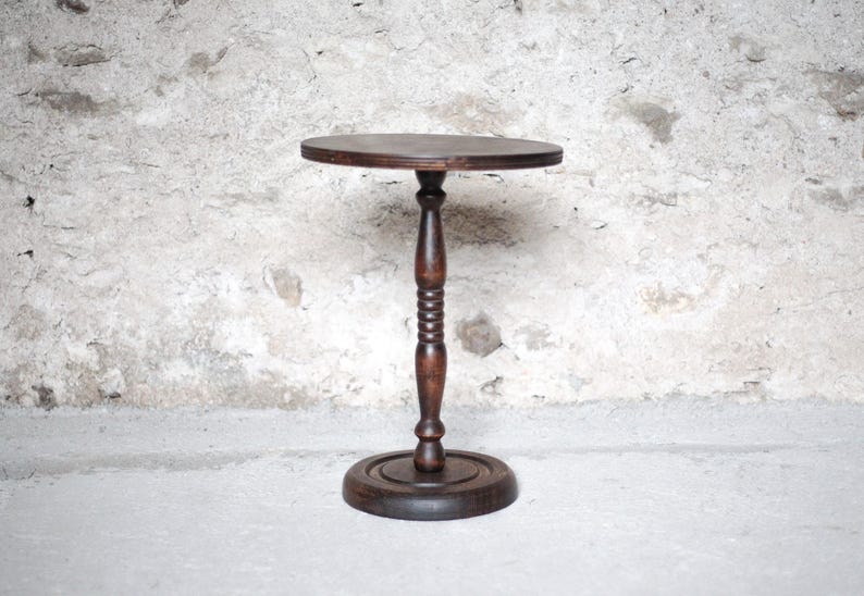 Pode incluir: Uma mesa de pedestal de madeira castanho-escura com um tampo circular, uma coluna central torneada com detalhes canelados decorativos e uma base redonda resistente. A mesa tem um acabamento liso e polido que real&ccedil;a os veios da madeira.