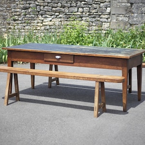 Peut inclure: Une table en bois rustique avec un plateau foncé et un tiroir. La table est soutenue par des pieds en tréteau et est associée à un banc en bois assorti.