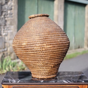 May include: A large, round, woven basket made of natural materials. The basket is brown and has a slightly textured surface. It is sitting on a black marble surface.