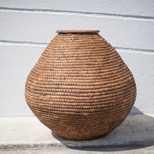 Puede incluir: Una cesta grande, redonda y marrón tejida con materiales naturales. La cesta está sobre una superficie de hormigón.