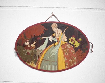 May include: A vintage oval-shaped wall hanging with a painted scene of a woman in a yellow and red dress offering a red rose to a man in a black mask. The background is a dark forest with red and green foliage.