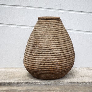 May include: A large, brown, woven basket with a rounded, teardrop shape. The basket is made of natural materials and has a rustic, handcrafted look.