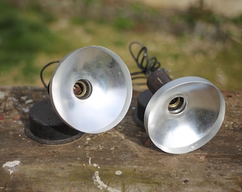 May include: Two silver metal lampshades with black electrical cords and a black base. Each lampshade has a round, silver metal socket.