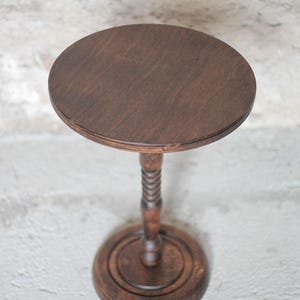 Pode incluir: Uma mesa de pedestal em madeira castanho-escura com um tampo circular, uma coluna central com um design torcido e uma base redonda escalonada. O veio da madeira &eacute; vis&iacute;vel na superf&iacute;cie plana do tampo e na base s&oacute;lida da mesa.