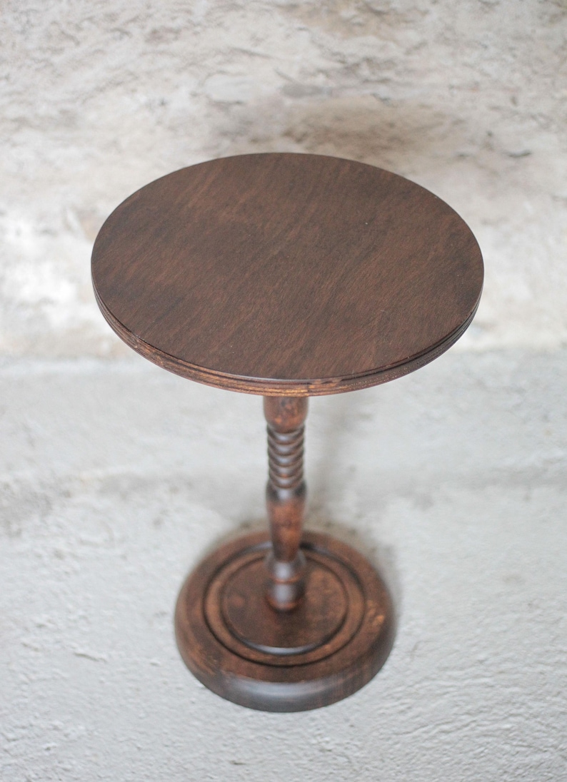 Pode incluir: Uma mesa de pedestal em madeira castanho-escura com um tampo circular, uma coluna central com um design torcido e uma base redonda escalonada. O veio da madeira &eacute; vis&iacute;vel na superf&iacute;cie plana do tampo e na base s&oacute;lida da mesa.