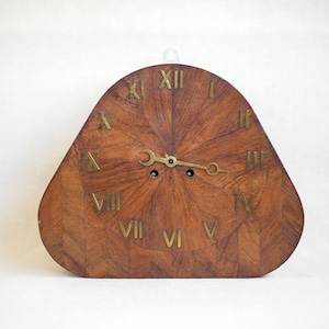May include: A wooden clock with Roman numeral markings on a brown wood face. The clock is shaped like a triangle with rounded edges.